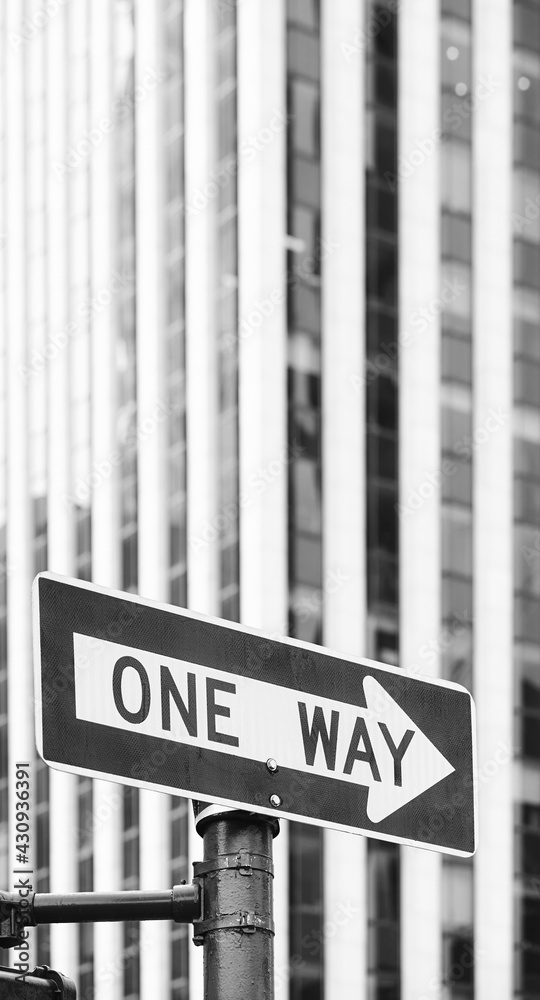 Obraz premium Black and white picture of a One Way traffic sign with blurred office building in background, selective focus, New York City, USA.