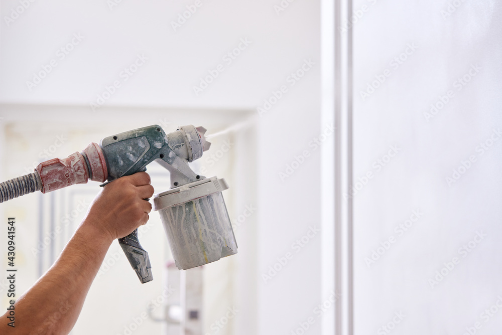 Worker painting wall with spray gun in white color. - obrazy, fototapety, plakaty 