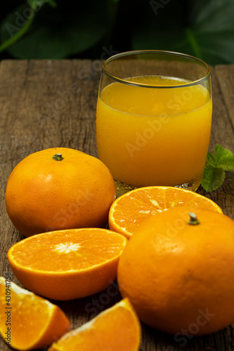 A glass of orange juice with orange fruit cut in half and orange slice on the wooden table.