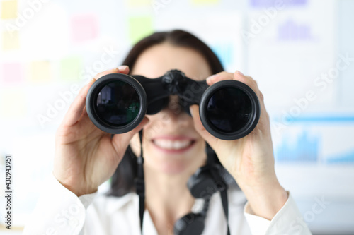 Woman looking in black professional binoculars in office closeup © H_Ko
