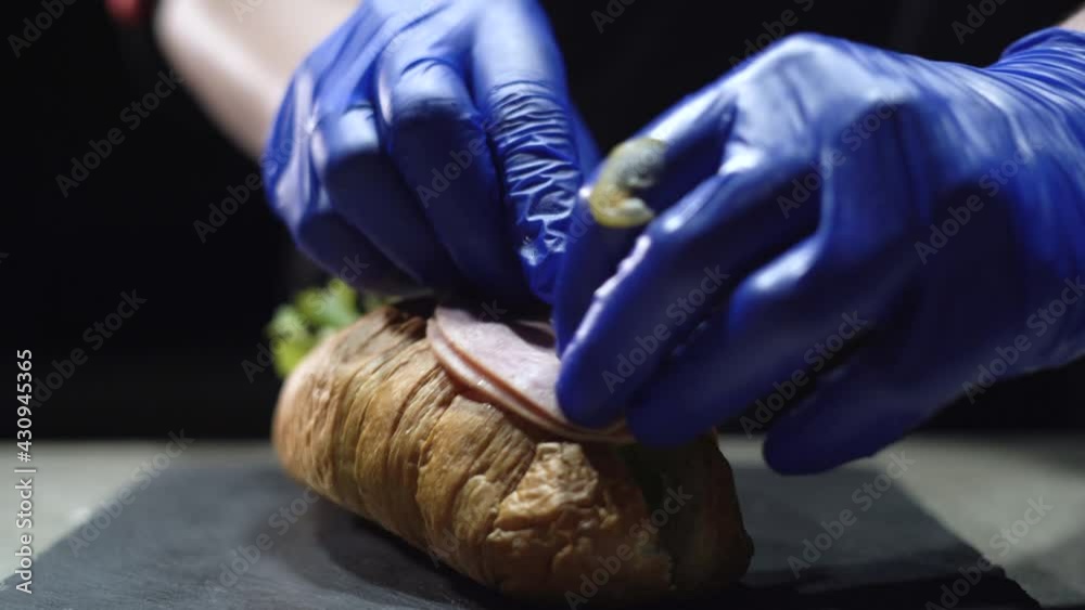 Close-up of a chef's hands in black gloves preparing a croissant sandwich. Fast breakfast. Take bacon and put it on a bun. Close-up of a chef's hands in black gloves preparing a croissant sandwich. Fast breakfast. Take bacon and put it on a bun.