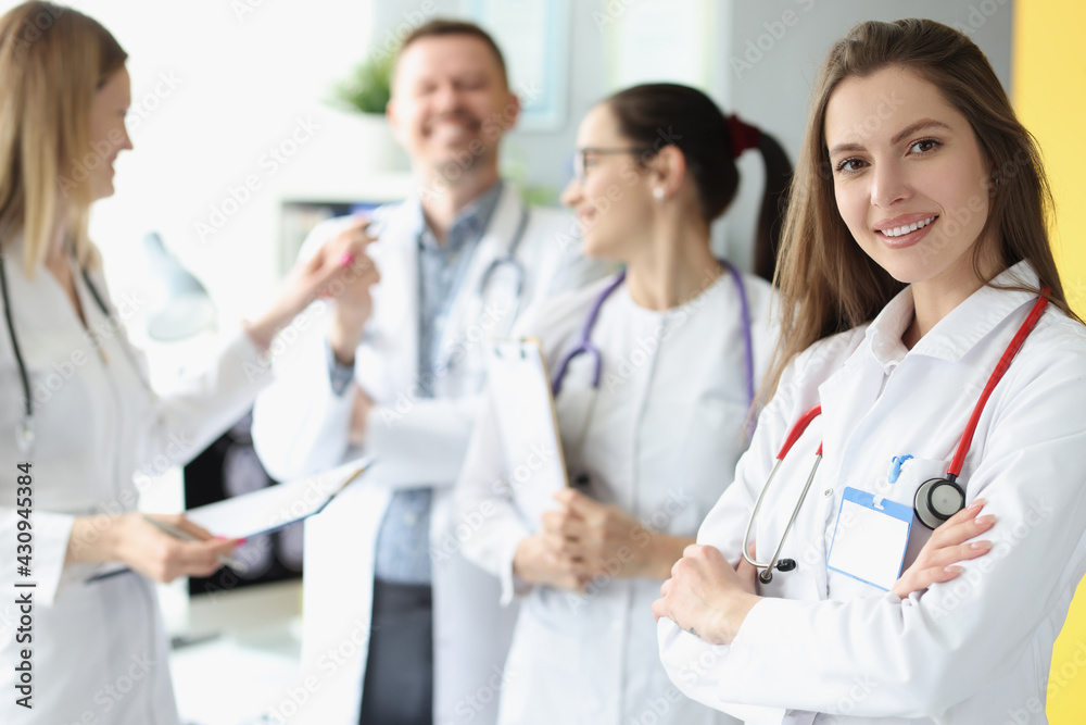 Smiling woman doctor with red stethoscope standing against background of colleagues Smiling woman doctor with red stethoscope standing against background of colleagues