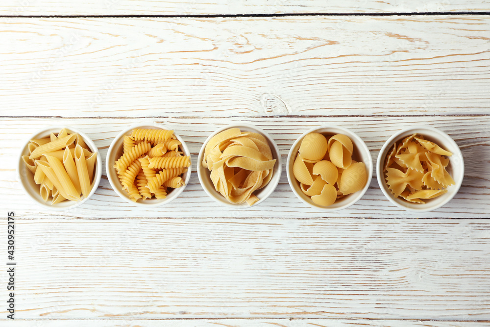 Bowls with uncooked pasta on white wooden background Bowls with uncooked pasta on white wooden background