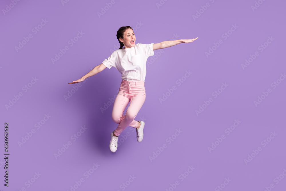 Full size photo of young girl happy positive smile jump up hands wings fly isolated over violet color background
