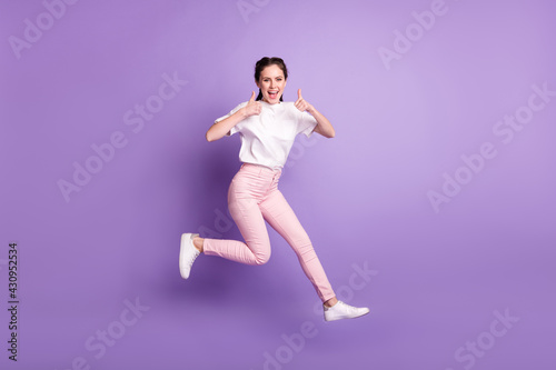 Full body photo of happy funky young woman jump up smile make thumbs up isolated on violet color background