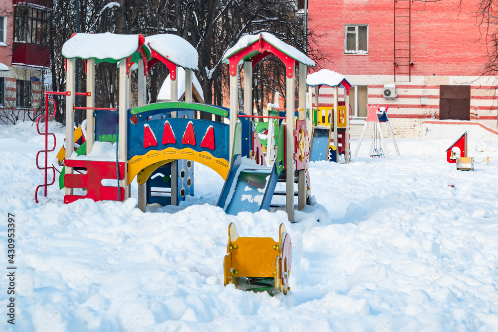 Naklejka premium The playground in the city's residential courtyard is built for the development and entertainment of children. The playground is covered with snow during the winter season.