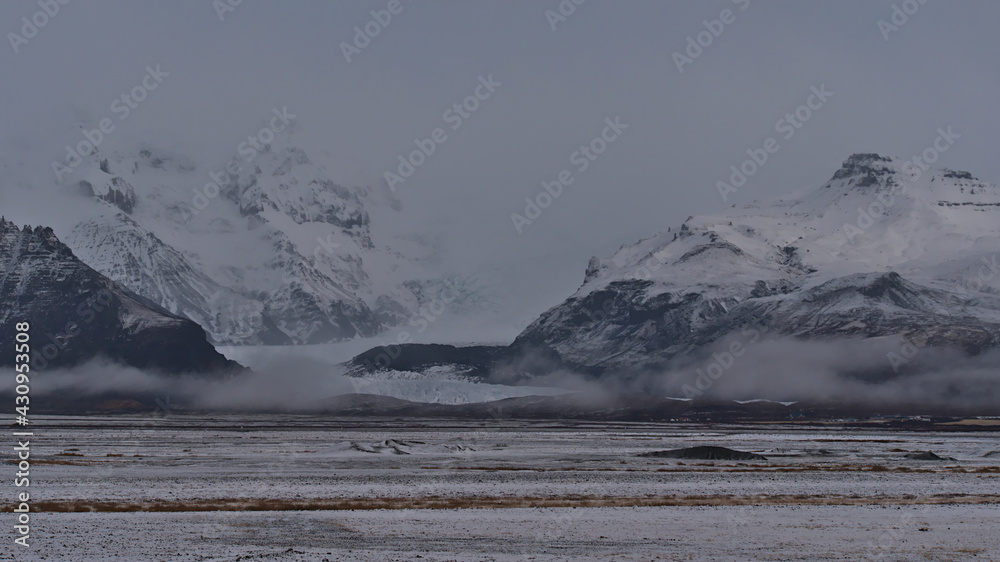 Beautiful view of snow-covered rough mountain range of Öræfajökull in the south of Iceland disappearing in the low clouds with Svínafellsjökull glacier, part of Vatnajökull ice cap, in winter season.