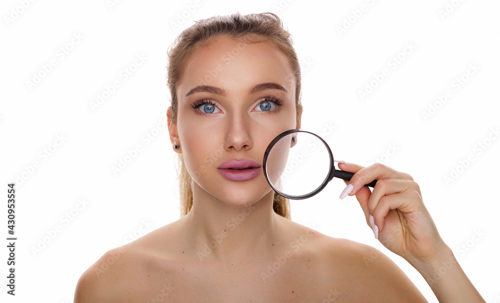 Youth and skin care concept. Beautiful face of young woman with clean fresh skin and blue eyes holds near the face magnifying glass looking at camera isolated on white background with copy space Youth and skin care concept. Beautiful face of young woman with clean fresh skin and blue eyes holds near the face magnifying glass looking at camera isolated on white background with copy space