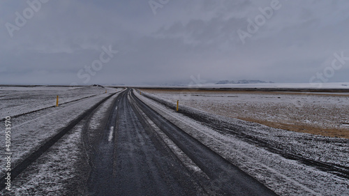 Sparse landscape with view of snow-covered ring road  route 1  in southern Iceland near Skaftafell on cloudy winter day in diminishing perspective with majestic Vatnaj  kull glacier in background.