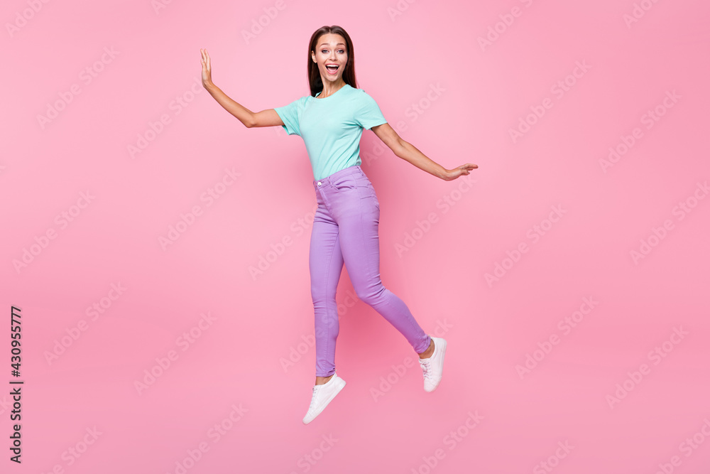Full size photo of young beautiful cheerful happy funny woman jumping wear violet pants isolated on pink color background Full size photo of young beautiful cheerful happy funny woman jumping wear violet pants isolated on pink color background