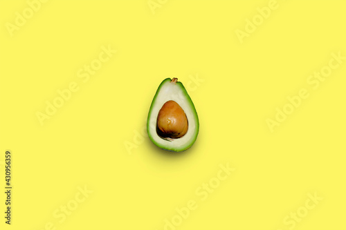 half an avocado in the center on a bright yellow background, top view