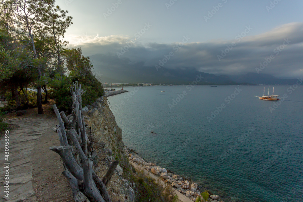 Sea view from the cliff. Evening landscape. Yacht on the sea. A path along the sea. Sunset on the sea. Wicker fence.Clouds at sunset.