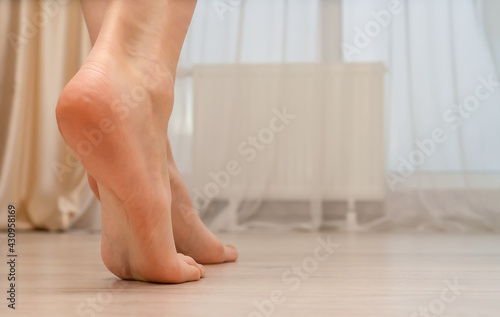 Close-up of a young woman's bare feet on a warm floor in a bedroom or living room. Women's bare feet walk in a room with an electric heated floor in a modern house. Copy space