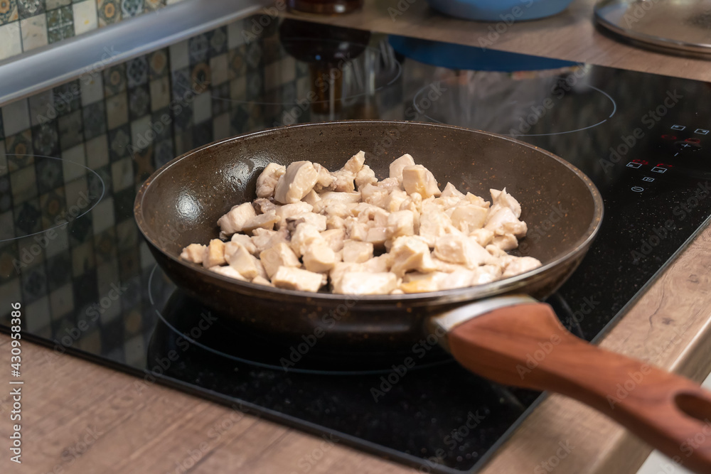 In a frying pan, pieces of chicken meat are fried on an induction stove close-up In a frying pan, pieces of chicken meat are fried on an induction stove close-up