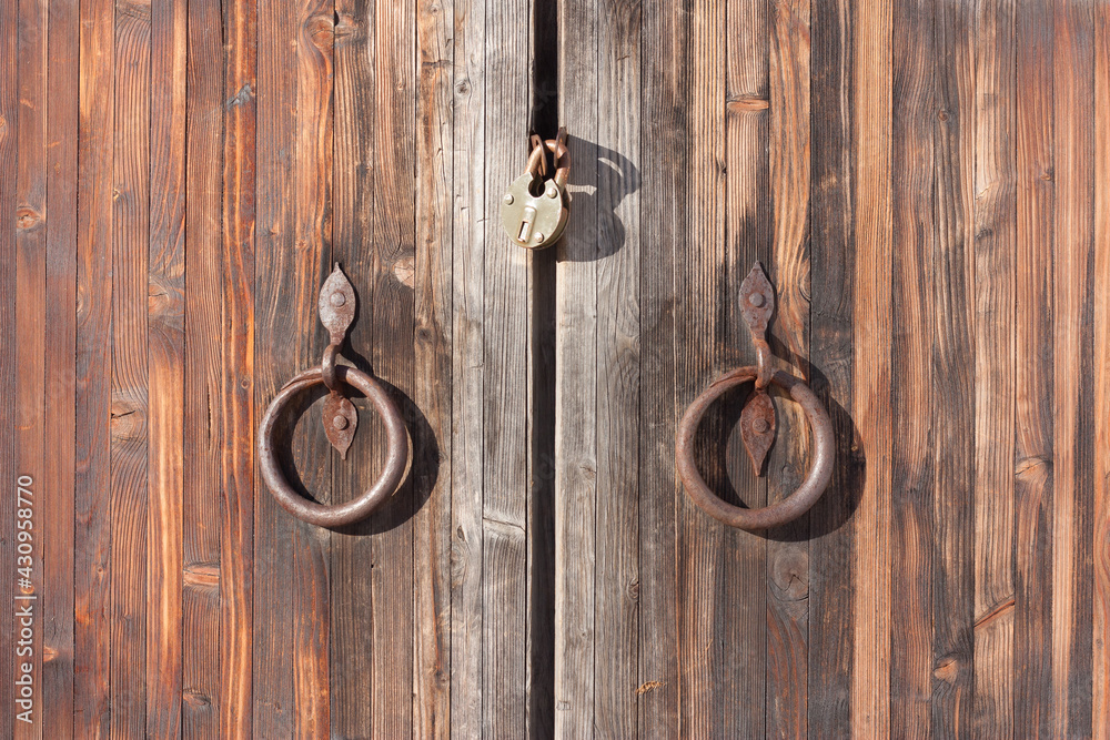 Fragment of an old wooden gate with a wrought iron handle with rust stains. Texture, background, symmetry. Fragment of an old wooden gate with a wrought iron handle with rust stains. Texture, background, symmetry.