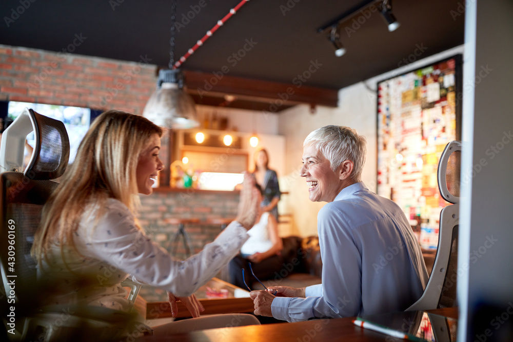 An elderly business woman is having a good time with her young female colleague while they are sitting at the office. Business, office, job An elderly business woman is having a good time with her young female colleague while they are sitting at the office. Business, office, job