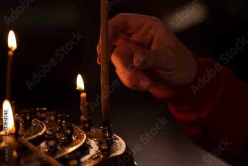 Batumi, Georgia - March 15, 2021: Woman's hand in a red jacket puts a church candle