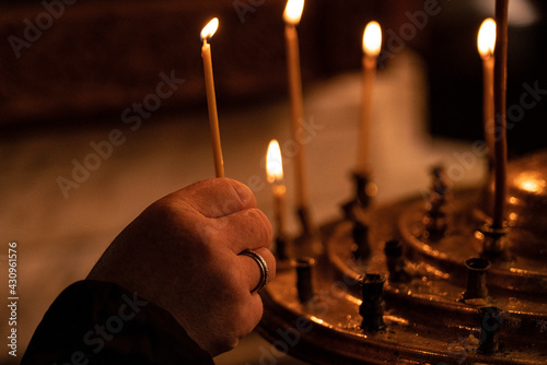 Batumi, Georgia - March 15, 2021: Woman's hand in a red jacket puts a church candle