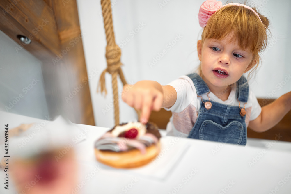 Fototapeta premium A little girl in a pastry shop is amazed by delicious donut. Pastry shop, dessert, sweet