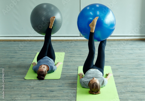 Beautiful two women doing yoga practice together. They lay down and playing with big ball tool. The concept for self-care sport and body balance