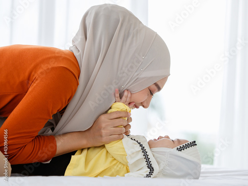 A cute and beautiful Asian Muslim in hijab dress kissing her baby daughter with a tender gesture. Love, care, and relationship concept