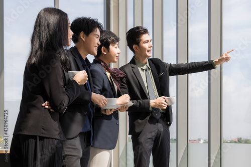 Group of variety LGBTQ, man and woman and transgender standing drinking coffee and taking and looking together to far point outside the office window