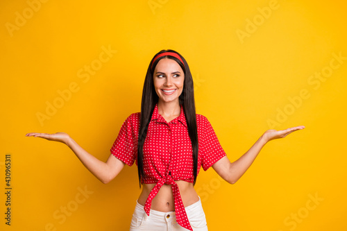 Portrait of attractive cheerful girl holding on palms two copy space variants vs ad isolated over bright yellow color background