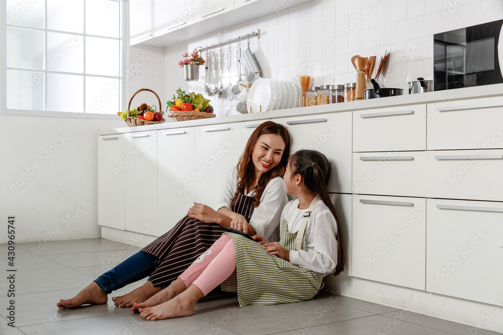 Asian mother and daughter happily sit and study how to make cakes from their laptops and smile in the kitchen at home.. Asian mother and daughter happily sit and study how to make cakes from their laptops and smile in the kitchen at home..