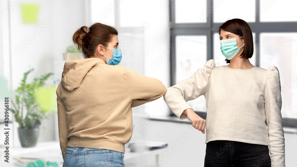 Fototapeta premium health protection, safety and pandemic concept - young women in masks meeting and making elbow bump greeting gesture over office background
