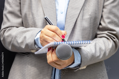 Female journalist at news conference or media event, writing notes, holding microphone