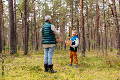 picking season, leisure and people concept - grandmother with smartphone photographing happy smiling grandson with mushrooms in basket in forest