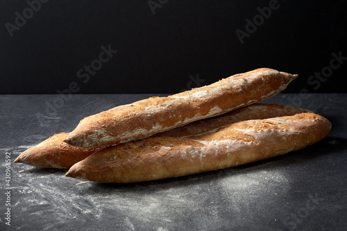food, baking and cooking concept - pile of baguette bread on table over dark background © Syda Productions