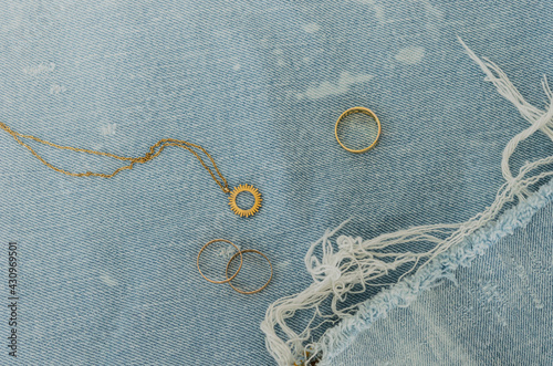 Bodegón con joyas de oro sobre tejido denim azul claro con manchas blancas y flecos deshilachados photo