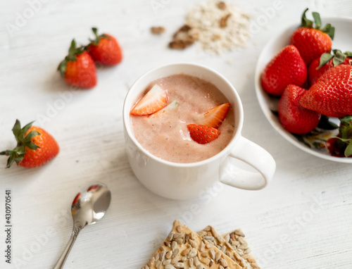 strawberry smoothie with strawberries in a white cup on a white wooden table, decorated with strawberries. Strawberries, cookies near the cocktail mug. Healthy and Vegetarian Breakfast Concept