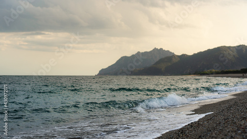 waves at a beach and mountains in the evening. Focus on foreground, blurry background with coastline.