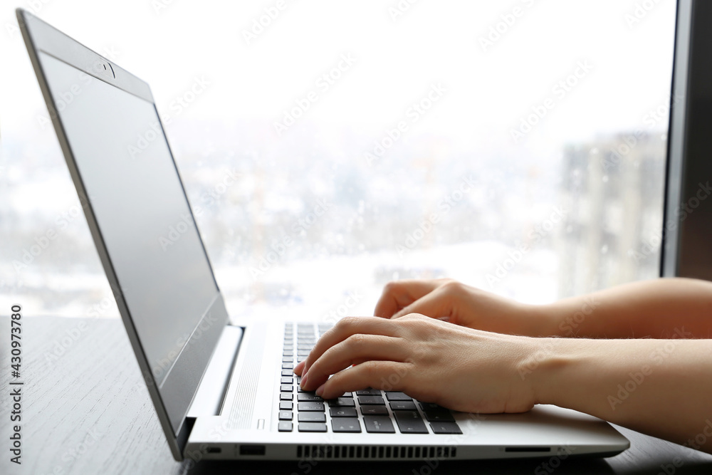 Woman sitting at laptop keyboard near the window in rainy weather, female hands closeup. Cozy workplace, concept of online communication, office or home work Woman sitting at laptop keyboard near the window in rainy weather, female hands closeup. Cozy workplace, concept of online communication, office or home work
