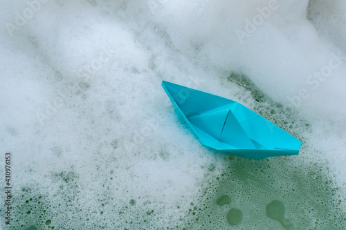 Origami in the form of a paper boat in soapy water in a bath