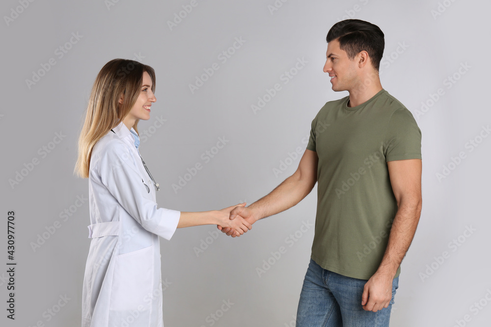 Doctor and patient shaking hands on light grey background Doctor and patient shaking hands on light grey background