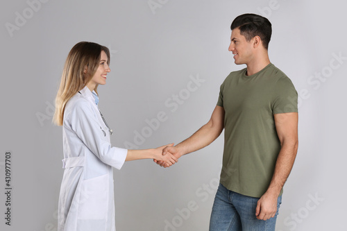 Doctor and patient shaking hands on light grey background