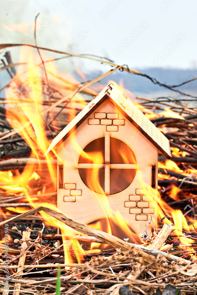 Burning dry grass next to a wooden house.Background. The toy house is on fire. the concept of insurance of investment risk of real estate or life fate