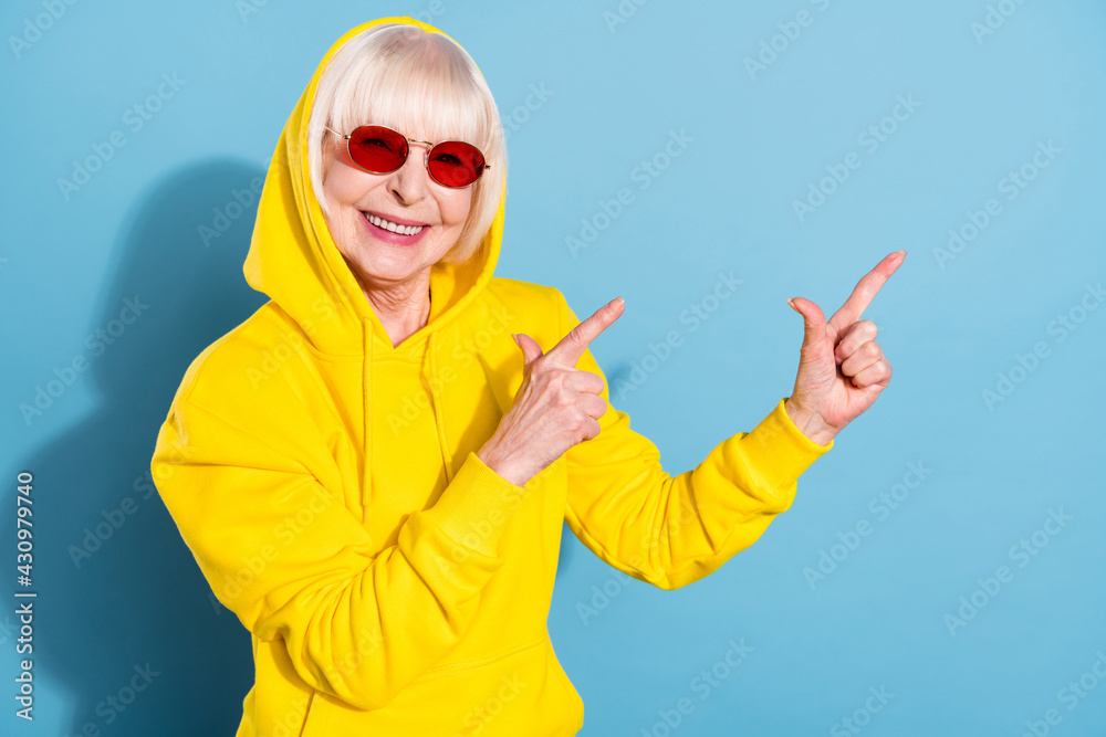 Photo of sweet nice pretty old woman point fingers empty space advert wear sunglass hoodie isolated on blue color background