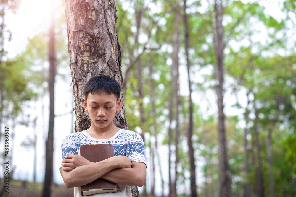 Christian boy pray to God with embrace Bible in forest, Focus face. Christian boy pray to God with embrace Bible in forest, Focus face.