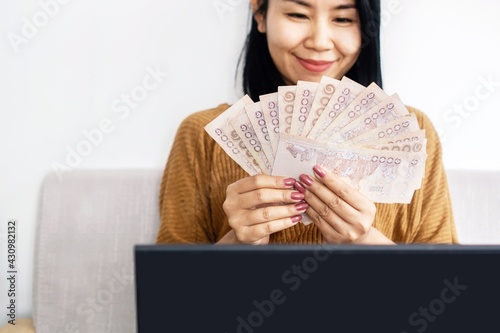 Fototapeta happy Asian business woman hand holding Thai baht banknotes setting on sofa , su