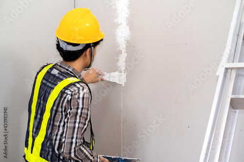 Construction worker plastering gypsum board or plasterboard panels wall with trowel. Home interior drywall works, renovation or construction