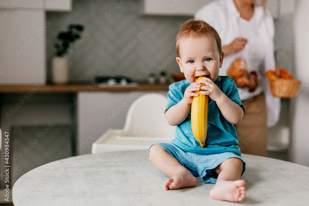 A little boy sits on the kitchen table with a banana in his hands and smiles A little boy sits on the kitchen table with a banana in his hands and smiles