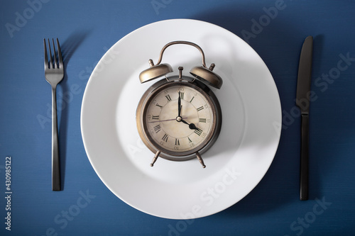 concept of intermittent fasting, ketogenic diet, weight loss. fork and knife, alarmclock on plate