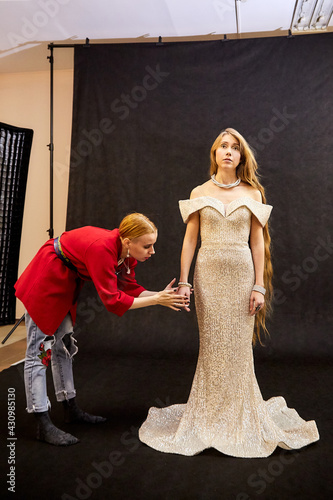 A costume designer or stylist helps a model prepare for a photo shoot in the studio