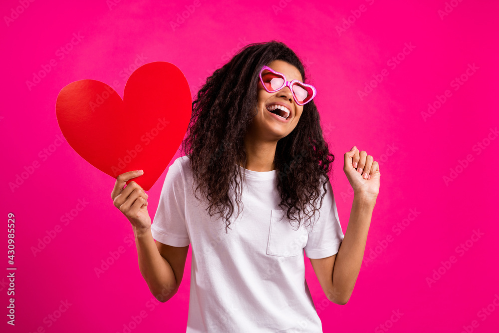 Photo of funny wavy millennial lady hold heart look empty space wear white t-shirt isolated on pink color background Photo of funny wavy millennial lady hold heart look empty space wear white t-shirt isolated on pink color background