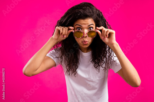 Photo of open-eyed wavy young lady touch spectacles wear white t-shirt isolated on pink color background
