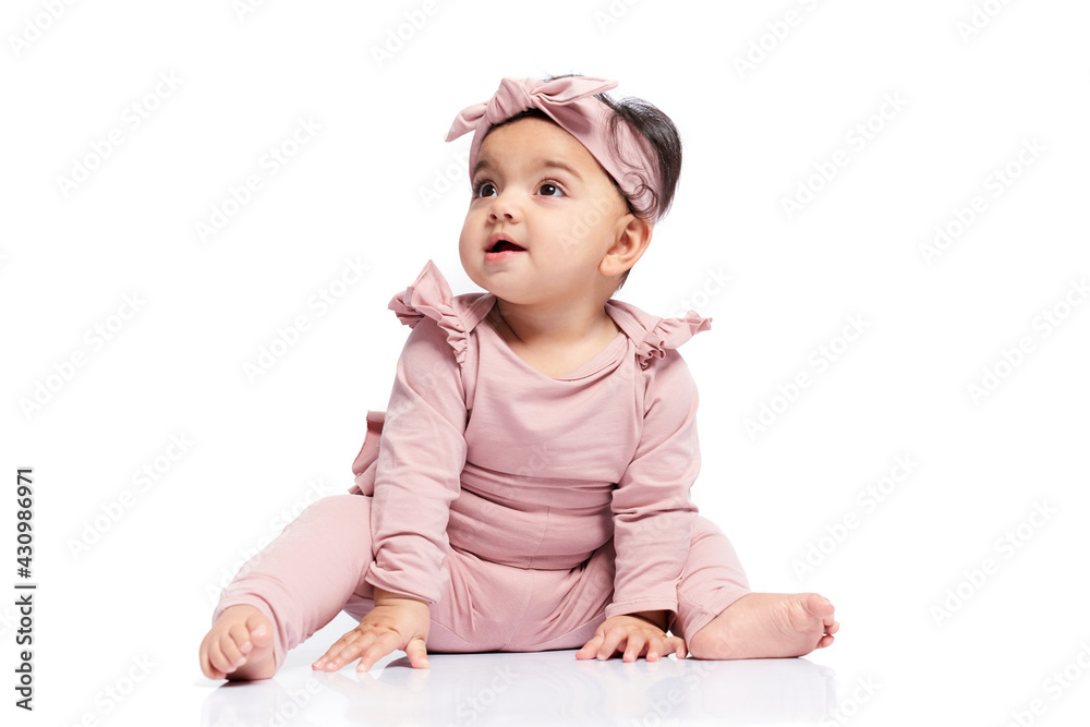 Cute baby girl in lovely pink outfit looking up with mouth open. Attractive little female kid sitting on floor and posing, isolated on white studio background. Concept of childhood. Cute baby girl in lovely pink outfit looking up with mouth open. Attractive little female kid sitting on floor and posing, isolated on white studio background. Concept of childhood.